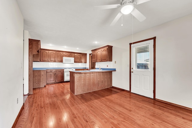 kitchen with kitchen peninsula, backsplash, ceiling fan, light hardwood / wood-style flooring, and range