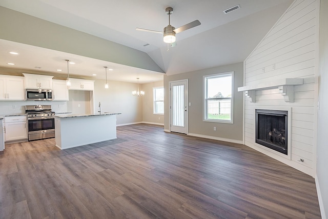 kitchen featuring appliances with stainless steel finishes, a large fireplace, dark wood-type flooring, pendant lighting, and white cabinets