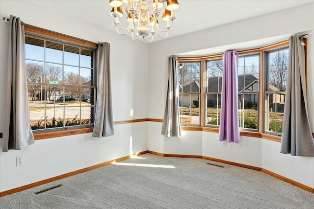 carpeted empty room featuring a healthy amount of sunlight and an inviting chandelier