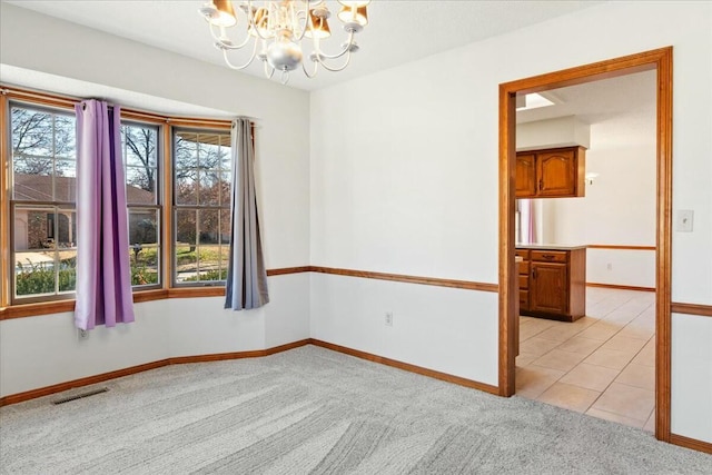 empty room with plenty of natural light, light colored carpet, and an inviting chandelier