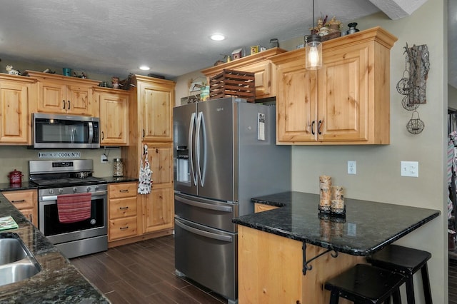 kitchen featuring a textured ceiling, stainless steel appliances, light brown cabinets, decorative light fixtures, and dark hardwood / wood-style floors