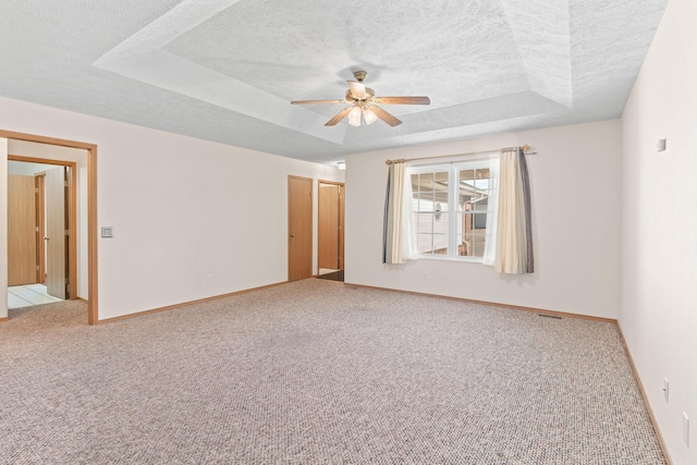 spare room with a textured ceiling, a tray ceiling, ceiling fan, and light colored carpet