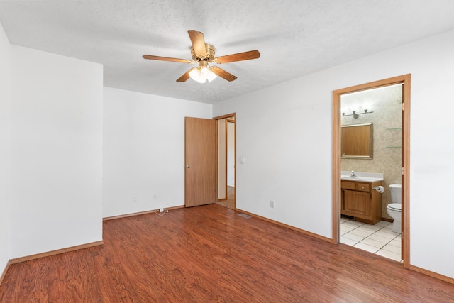 unfurnished bedroom featuring ensuite bathroom, light hardwood / wood-style floors, a textured ceiling, and ceiling fan