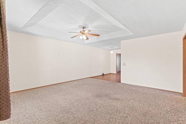 empty room with carpet flooring, a textured ceiling, a raised ceiling, and ceiling fan