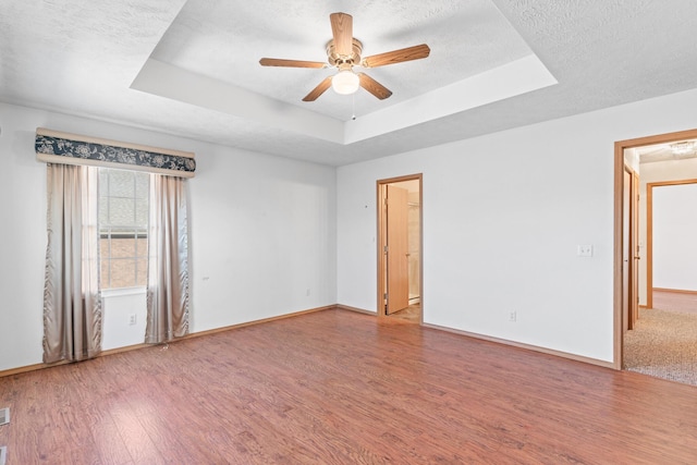 empty room featuring wood-type flooring, a textured ceiling, a tray ceiling, and ceiling fan