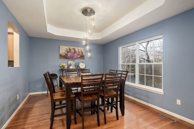 dining area with a raised ceiling and wood-type flooring