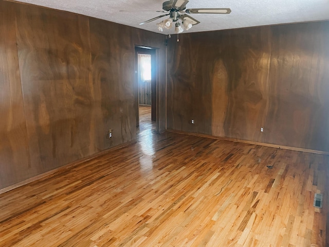 spare room with wood walls, ceiling fan, light hardwood / wood-style floors, and a textured ceiling