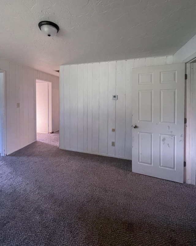 unfurnished room with wood walls, carpet floors, and a textured ceiling