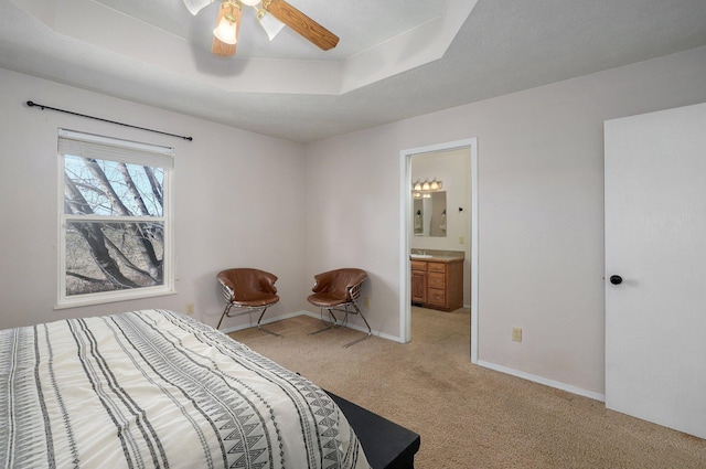 bedroom featuring a raised ceiling, connected bathroom, ceiling fan, and light carpet