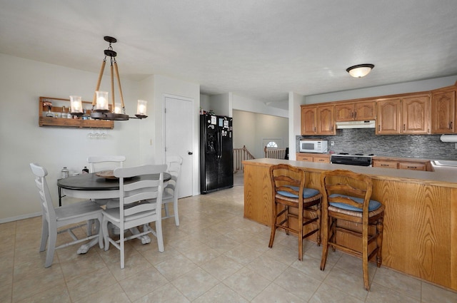 kitchen featuring kitchen peninsula, decorative backsplash, black appliances, pendant lighting, and a chandelier