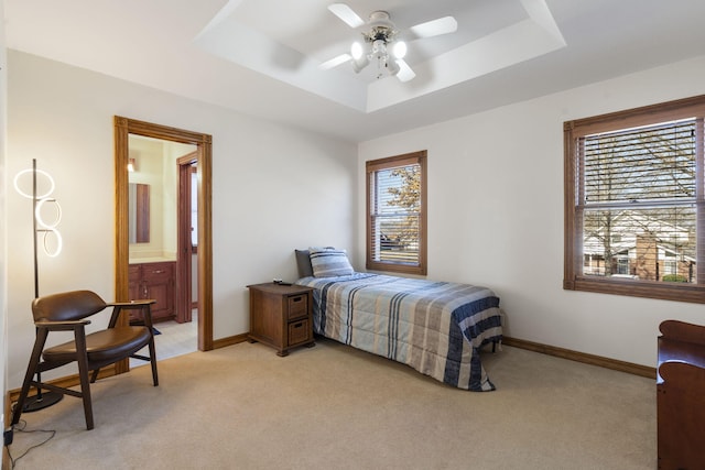 bedroom with a raised ceiling, connected bathroom, ceiling fan, and light colored carpet