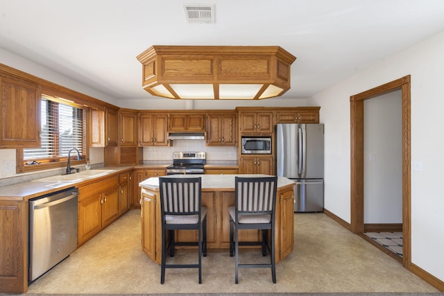 kitchen with appliances with stainless steel finishes, backsplash, sink, a kitchen island, and a breakfast bar area