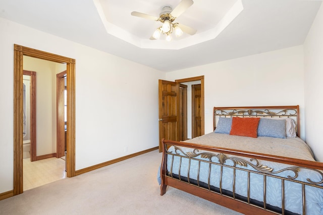 carpeted bedroom featuring connected bathroom, a tray ceiling, and ceiling fan