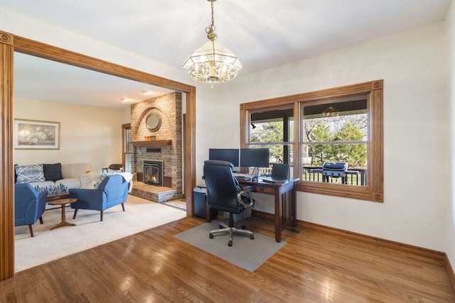 office with hardwood / wood-style floors, a brick fireplace, and a chandelier