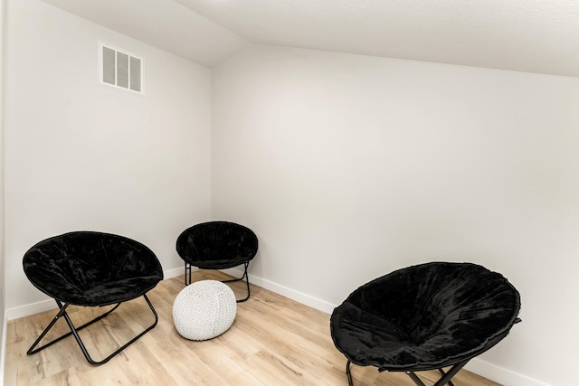 sitting room featuring visible vents, baseboards, light wood-style flooring, and vaulted ceiling