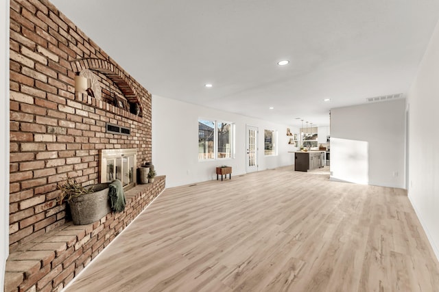 unfurnished living room featuring light wood finished floors, visible vents, recessed lighting, and a brick fireplace