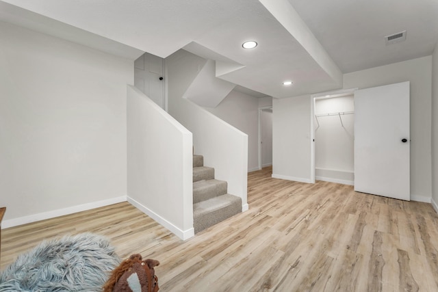 finished below grade area with visible vents, stairway, baseboards, and wood finished floors