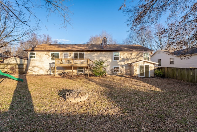 back of house with fence, an outdoor fire pit, a chimney, a yard, and a deck