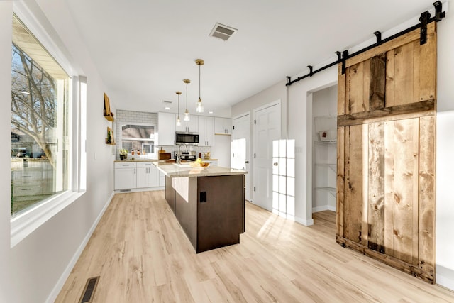 kitchen featuring light wood-style flooring, white cabinetry, stainless steel appliances, and a barn door