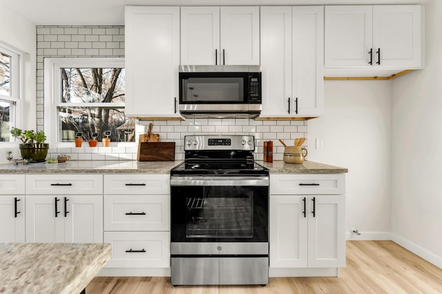 kitchen featuring baseboards, light wood-style floors, appliances with stainless steel finishes, white cabinetry, and backsplash