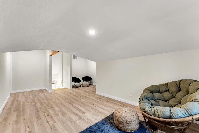 living area with visible vents, light wood-style flooring, baseboards, and vaulted ceiling