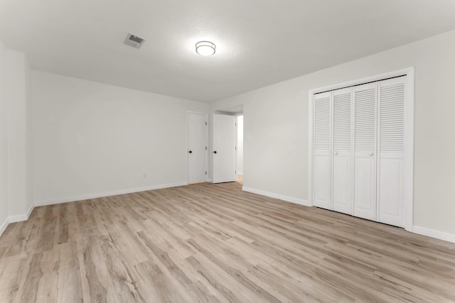 unfurnished bedroom featuring light wood-style floors, visible vents, a closet, and baseboards