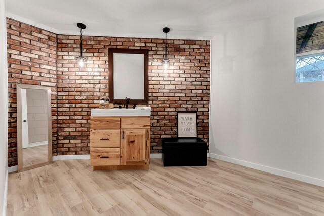 bathroom featuring vanity, wood finished floors, baseboards, and brick wall