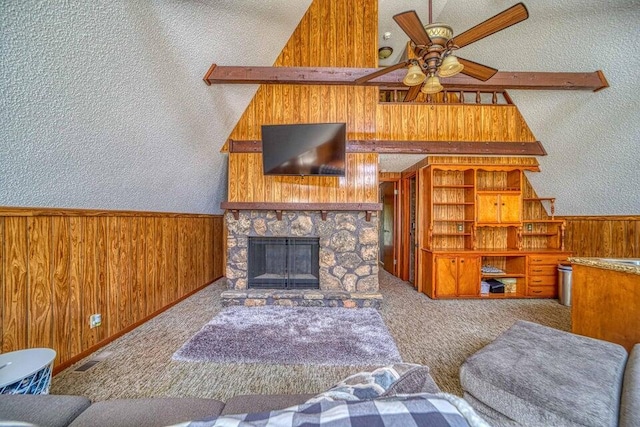 living room with carpet, wooden walls, ceiling fan, a fireplace, and a textured ceiling