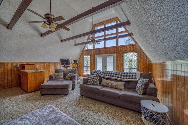 carpeted living room with french doors, lofted ceiling with beams, wooden walls, ceiling fan, and a textured ceiling