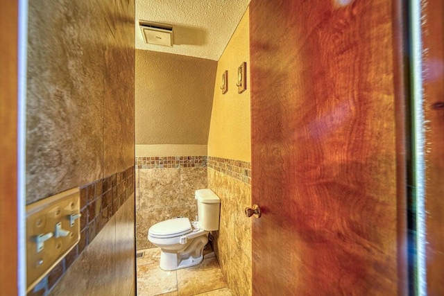 bathroom featuring a textured ceiling, toilet, tile walls, and a mail area