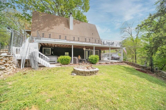 rear view of property with a wooden deck, a fire pit, a patio, a hot tub, and a lawn