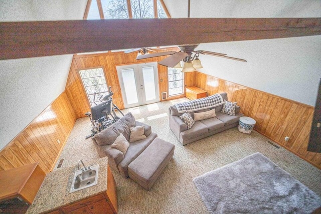 carpeted living room with beam ceiling, wooden walls, ceiling fan, and a healthy amount of sunlight