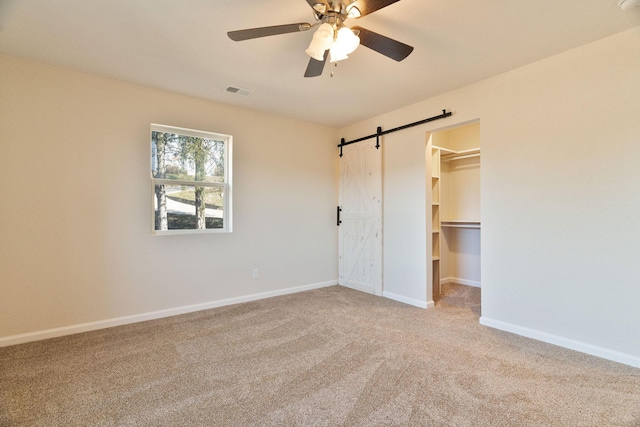 unfurnished bedroom featuring light carpet, ceiling fan, a barn door, a spacious closet, and a closet