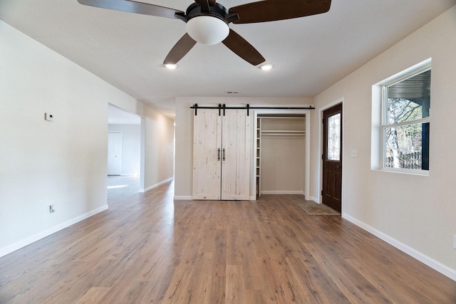 unfurnished bedroom featuring ceiling fan, a barn door, wood-type flooring, and a closet