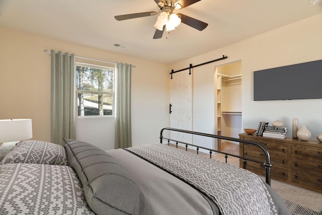 carpeted bedroom with ceiling fan, a barn door, a spacious closet, and a closet