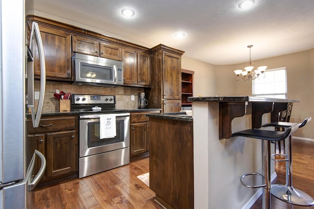 kitchen featuring pendant lighting, a center island, appliances with stainless steel finishes, dark hardwood / wood-style flooring, and a chandelier