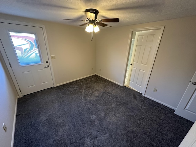 entrance foyer with ceiling fan, a textured ceiling, and dark colored carpet