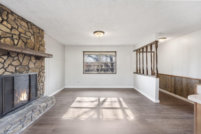 unfurnished living room with a textured ceiling, a stone fireplace, and dark hardwood / wood-style floors