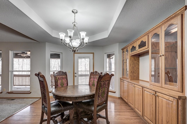 dining room with ceiling fan with notable chandelier, light wood-type flooring, a textured ceiling, and a tray ceiling