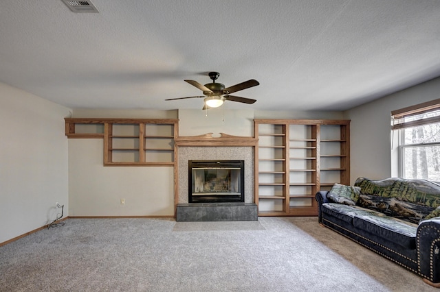 living room with ceiling fan, carpet floors, a textured ceiling, and a tiled fireplace