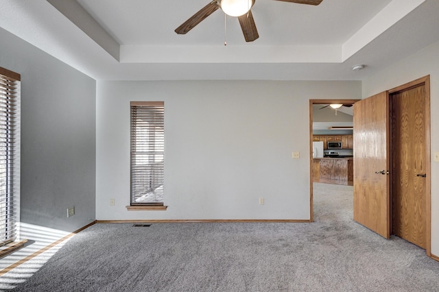 carpeted empty room featuring ceiling fan and a raised ceiling