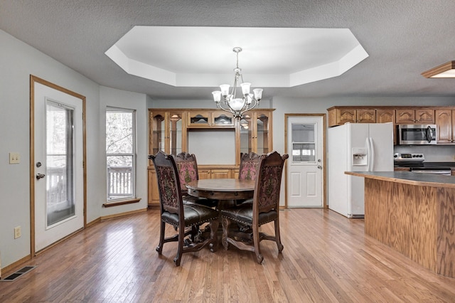 dining area with a tray ceiling, light hardwood / wood-style flooring, and an inviting chandelier