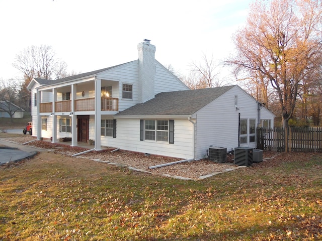 back of property with cooling unit, a balcony, and a yard