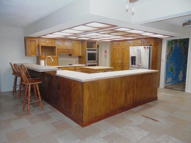 kitchen featuring a kitchen breakfast bar, sink, appliances with stainless steel finishes, tasteful backsplash, and kitchen peninsula