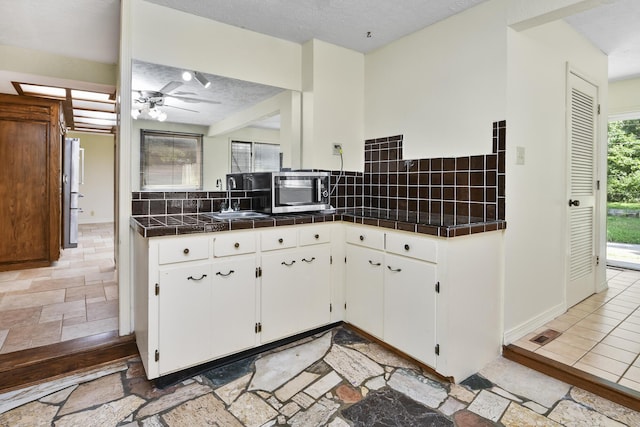 3011 E Lamonta Dr, Springfield, MO 65804 - kitchen with decorative backsplash, a ceiling fan, white cabinetry, tile countertops, and a textured ceiling