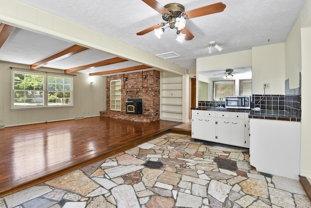 3011 E Lamonta Dr, Springfield, MO 65804 - unfurnished living room featuring a wood stove, light wood-style floors, ceiling fan, a textured ceiling, and beamed ceiling