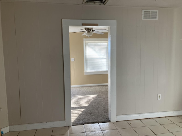 interior space with wood walls, light tile patterned flooring, a baseboard heating unit, and ceiling fan