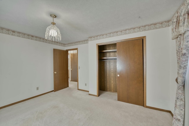 unfurnished bedroom featuring a textured ceiling, light colored carpet, an inviting chandelier, and a closet