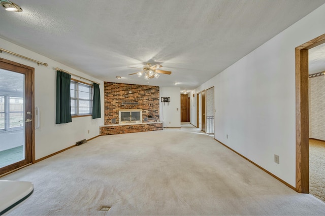 unfurnished living room with a textured ceiling, light colored carpet, a brick fireplace, and ceiling fan