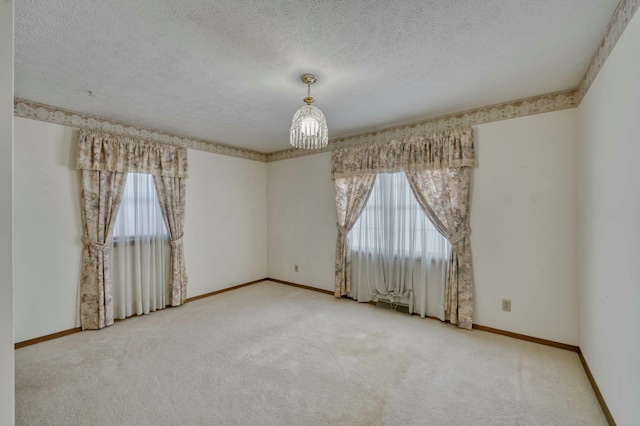 spare room featuring a textured ceiling, carpet floors, and a notable chandelier